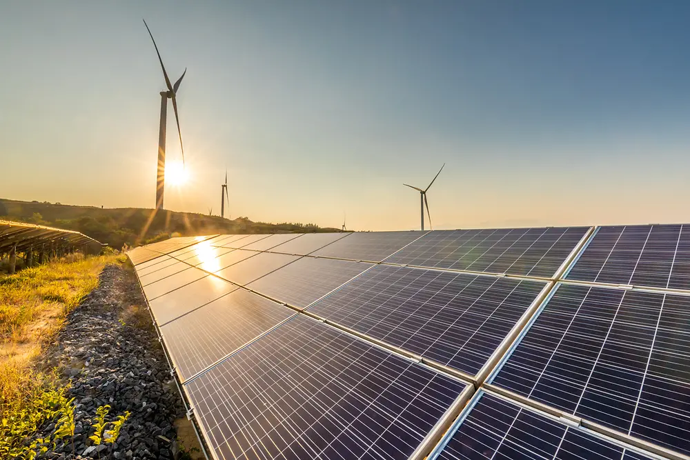 Solar panels at sunset with a windmills in the background